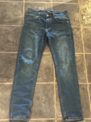 Blå slim fit jeans från Replay - Ny pris 1200 kr: Vårt pris 450! Snygga blå slim fit jeans från Replay med klassisk femficksmodell och diskreta slitningar. Jeansen har normal midja, dragkedjegylf och är tillverkade i ett mjukt denimtyg som sitter skönt hela dagen. Den är 150 cm lång passar dom flesta barn. 😃🏅