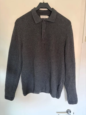 Grå stickad tröja med krage - Mysig grå stickad tröja med klassisk krage och tre knappar framtill. Tröjan har lång ärm och är ribbstickad för extra struktur. Perfekt för kyliga dagar och enkel att matcha med olika outfits. Tröjan kommer från Casual Friday och är endast använd 2-3ggr. Jag säljer eftersom den är för liten och får ingen användning för den. Storleken är M passar S/M. Nypris är 899:-