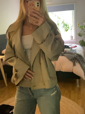 Beige kort trenchcoat  - Säljer en beige, kort trenchcoat med bred krage och dubbelknäppning. Jackan är använd men i bra skick! 