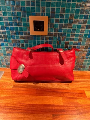 Röd handväska  - Röd handväska med dubbla handtag. Väskan har en dragkedja upptill och en praktisk ytterficka med dragkedja på baksidan. Perfekt för dig som vill ha en färgklick till din outfit. Lite solkigt foder med det går säkert att få bort. Mått 36x17x8cm.