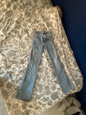 Ljusblå bootcut jeans - Säljer ett par ljusblå bootcut jeans med klassisk femficksdesign och låg midja. Jeansen har utsvängda ben och är tillverkade i ett mjukt denimtyg som ger en avslappnad och trendig look. Perfekta för dig som gillar retrostil och vill ha ett par bekväma jeans.