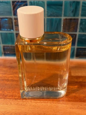 Burberry London Dream, edp 30ml - Burberry London Dream, edp, 30ml, endast använd ett par ggr, som ny! Säljer en elegant parfym i en rektangulär glasflaska med vit kork. Doften har fräscha toppnoter av citron och ingefära, blommiga hjärtnoter av pion och ros samt basnoter av mysk och amber. Flaskan är genomskinlig och stilren, perfekt för dig som gillar fräscha och blommiga dofter.