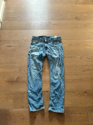 Blå raka jeans med slitningar - Säljer ett par blå jeans med raka ben och snygga slitningar framtill. Jeansen har klassisk femficksdesign och knappgylf. Perfekta för en avslappnad och trendig look. Materialet är denim i bomull.