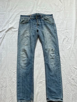 Blåa jeans från Dondup  - Säljer ett par blå jeans med rak passform och slitna detaljer på både fram- och baksida. Jeansen har klassiska fem fickor och dragkedjegylf. Materialet är denim i bomull och färgen är ljusblå med tvättade partier.