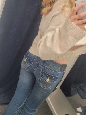 True religion jeans - Säljer ett par blå bootcut jeans med snygga fickdetaljer och guldknappar bak. Jeansen har låg midja och klassisk femficksdesign.  Perfekta för dig som vill ha en trendig och avslappnad stil.Har ett litet märke som man ser på sista bilden men inget som stör.