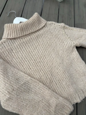 Beige stickad polotröja - Mysig beige stickad polotröja med grovstickad struktur och lång ärm. Tröjan har en hög krage och ribbstickade muddar vid hals och ärmslut. Perfekt för kalla dagar och enkel att matcha med olika outfits. Tröjan har en guldig söm vid vissa ställen! 🤩