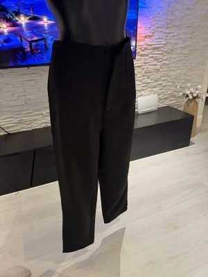 Svarta raka kostymbyxor - Säljer ett par svarta kostymbyxor med rak passform och hög midja. Byxorna har klassisk design med diskret knapp- och dragkedjestängning framtill. Perfekta för en stilren och clean look.