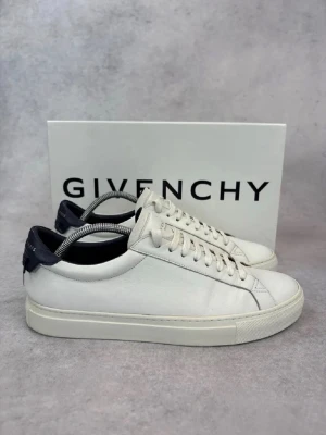 Vita Givenchy sneakers i läder - Snygga vita sneakers från Givenchy i slimmad low-top modell. Skorna är tillverkade i slätt läder med mörkblå detalj på hälen där Givenchy-loggan syns. Klassisk snörning och vit sula ger en clean och stilren look. Ca 28 cm skosula. Ställ frågor!