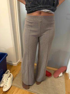Grå ribbade mjukisbyxor med raka ben - Säljer ett par grå mjukisbyxor med ribbad struktur och raka, vida ben. Byxorna har hög midja och markerad söm framtill för en snygg look. Perfekta för chill dagar eller när du vill vara bekväm men ändå se stilren ut.