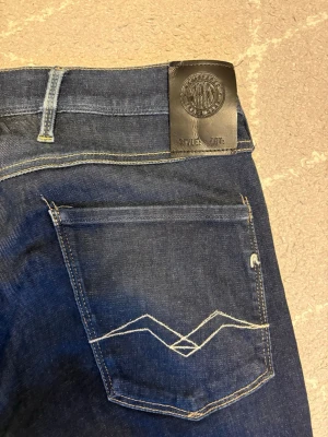 Blås replay anbass  - Snygga mörkblå jeans med raka ben och kontrastsömmar. Bakfickan har ett unikt broderat mönster och det finns en svart patch i midjan. Klassisk femficksmodell i denim som passar till det mesta.