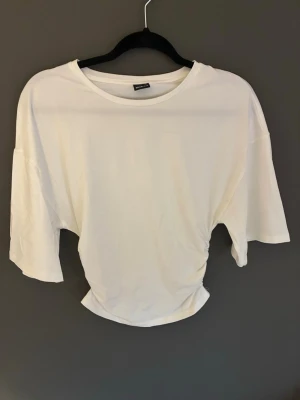 Vit croppad t-shirt med loose fit från Gina Tricot  - Säljer en vit croppad t-shirt med loose passform och korta ärmar. T-shirten har en enkel design med rund halsringning och är tillverkad i mjuk bomull. Perfekt för en avslappnad och trendig stil.