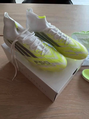 Adidas F50 Sparkfusion Elite - Adidas F50 Sparkfusion Elite FG/A fotbollsskor i stl 42, vita med neongula detaljer. Skorna ligger i originalkartong och har utbytbara sulor och skosnören samt en liten påse till. Helt nya, endast prövade en gång. Otroligt fin design som får dig verkligen att  sticka ut på planen. Nypris runt 2000, säljer för 1100, kom med bud behöver plats!