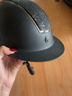 Svart ridhjälm med glitterdetalj - Svart ridhjälm med glitter, skjusterbar och fungerande skick förutom att det är lite repor i den som man ser på bild 