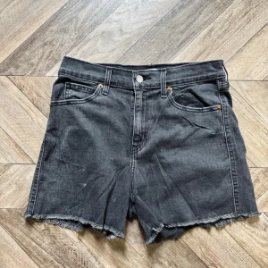 Svarta high-rise shorts Levi's - Snygga svarta high-rise shorts från Levi's med råa kanter och klassisk femficksdesign. Gjorda i slitstark denim med knapp och dragkedja framtill. Perfekta för en avslappnad och trendig look.