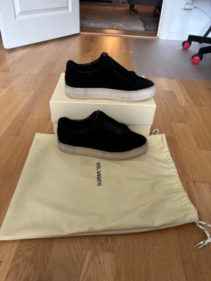 Lacceles Axel arigato skor - Stilrena svarta sneakers från Axel Arigato i sammet med tjock vit sula. Skorna har en minimalistisk design utan synliga snören och en låg silhuett. Perfekta för dig som gillar en clean och modern look.