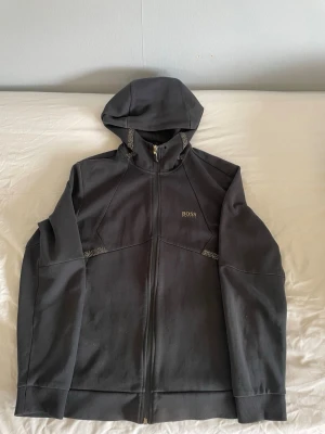 Svart Hugo Boss Zip Up - Snygg svart hoodie från BOSS med dragkedja framtill och huva. Diskret BOSS-logga på bröstet och coola detaljer längs sömmarna. Tillverkad i mjukt material som känns skönt mot huden. Perfekt för en avslappnad och stilren look.