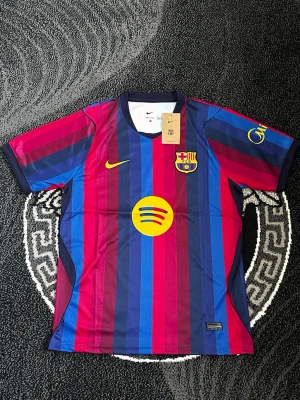 Barcelona matchtröja Nike blå/röd - Säljer en officiell FC Barcelona matchtröja från Nike med klassiska blå och röda vertikala ränder. Tröjan har klubbmärke, Nike-logga och Spotify-logga på bröstet samt korta ärmar och rund hals. Perfekt för dig som älskar fotboll och vill stötta Barca.
