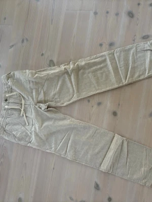 Beige linnebyxor med dragsko HM - Snygga beige linnebyxor med avslappnad passform och elastisk midja med dragsko. Byxorna har raka ben och sidofickor, perfekta för en chill och stilren look. Tillverkade i ett lätt och luftigt linnematerial.