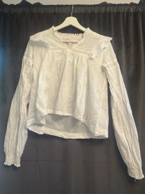 Vit romantisk blus med volangkrage - Säljer en vit blus med volangkrage och spetsdetaljer. Blusen har långa puffärmar med smock vid ärmslut och en lös, luftig passform. Perfekt för dig som gillar en romantisk och vintageinspirerad stil.