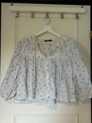 Vit blommig blus med v-ringning - Söt och luftig vit blus med ljuslila blommönster, v-ringning och knappar framtill från Gina Tricot i stl XS. Inga defekter vad jag kan se!