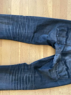 Mörkblå smala jeans med slitningar - Säljer ett par mörkblå jeans med smal passform och snygga slitningar på både fram- och baksida. Jeansen har klassiska fem fickor och kontrastsömmar. Materialet är denim med stretch för extra komfort. Perfekta för en avslappnad och trendig look.