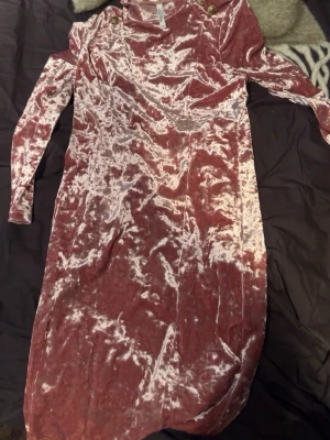 Rosa sammetklänning med axelknappar - Säljer en snygg rosa sammetklänning med lång ärm och dekorativa knappar på axlarna. Klänningen har en mjuk, glansig yta och en kroppsnära passform som ger en trendig look.