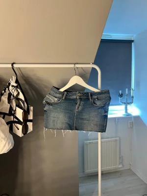 Ltb jeans kjol - Trendig blå jeanskjol med klassisk femficksdesign och rå, fransig nederkant. Kjolen har dragkedja och knapp framtill samt bälteshällor. Perfekt för en avslappnad och cool stil.