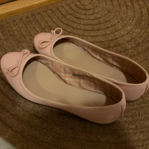 Ljusrosa ballerinaskor med rosett - Söta ljusrosa ballerinaskor med rund tå och dekorativ rosett framtill. Skorna har en klassisk, enkel design och är tillverkade i ett slätt material som ger en stilren look. Perfekta för dig som gillar en feminin och stilren stil. Skorna är i strl 39. 