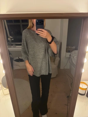 Grå oversized stickad tröja - Mysig grå stickad tröja med oversized passform och trekvartsärmar. Tröjan har en rund halsringning och är tillverkad i ett mjukt material som ger en avslappnad look. Perfekt att slänga på sig för en chill och stilren outfit.