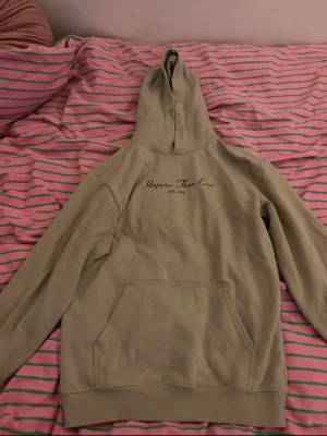 Hoodie Happier Than Ever - Säljer en beige hoodie med texten 'Happier Than Ever Billie Eilish' tryckt på bröstet. Hoodien har stor huva och magficka framtill. Perfekt för dig som gillar enkel stil och vill ha något bekvämt och snyggt.🥂