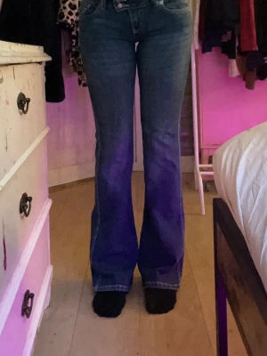 Blå bootcut jeans med broderad ficka - Säljer ett par blå bootcut jeans med snygg broderad detalj på bakfickan. Jeansen har hög midja och klassisk femficksmodell. Materialet är denim med lätt tvättad look och kontrastsömmar. Perfekta för dig som gillar en retro vibe!