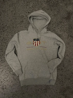 Grå Gant hoodie - Tjenare. En grå gant hoodie sådär använd men ändå i riktigt gott skick. Stil ren guldig text och komplett. Passar till en massa stilar och är riktigt schysst. Storlek S