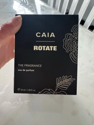 CAIA Rotate Eau de Parfum 50 ml - Säljer en CAIA Rotate Eau de Parfum i 50 ml flaska. Parfymen kommer i en elegant fyrkantig glasflaska med vit, oval kork och stilren svartvit etikett. Förpackningen är svart med vita detaljer och grafiskt bladmotiv. Perfekt för dig som gillar exklusiva dofter.