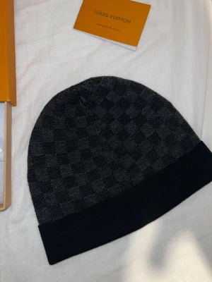 Louis Vuitton svart mössa med rutmönster - Snygg svart mössa från Louis Vuitton med klassiskt rutmönster och vikbar kant. skick 10/10 ingen konstig med blåa och svarta och om man vill ha en bara funkar kontakta mig gärna 