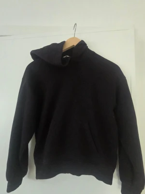 Svart hoodie från H&M - En enkel och stilren svart hoodie från H&M med klassisk huva och magficka. Tillverkad i mjukt bomullsmaterial som är skönt mot huden. Perfekt för dig som gillar en avslappnad och clean look.