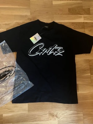 Svart Corteiz t-shirt med tryck - Snygg svart t-shirt från Corteiz med stort vitt grafiskt tryck på bröstet. Klassisk passform och rund hals. Perfekt för dig som gillar streetwear och vill sticka ut med en clean look. Står M fast passar för S