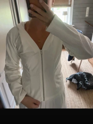 Vit hoodie med dragkedja och huva - Snygg vit hoodie med dragkedja framtill och huva. Figurnära passform och långa ärmar. Perfekt för en clean och stilren look. Tillverkad i ett mjukt material som känns skönt mot huden.
