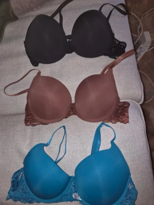 3-pack push up bhar spetsdetaljer - Säljer ett 3-pack bhar i svart, brun/röd och blå färg. Alla bhar har vadderade kupor och fina spetsdetaljer på sidorna och baktill. Axelbanden är justerbara och knäppningen sitter bak. Alla är storlek 75b