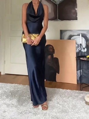 Balklänning/ bröllopsklänning  - Elegant marinblå långklänning i glansigt material med halterneck och djup urringning. Klänningen har en smickrande passform och öppen rygg, perfekt för en snygg och sofistikerad look. Den är bara använd en kväll den är helt ny