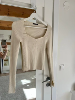  Beige långärmad topp - En ribbad topp i beige med lång ärm och fyrkantig ringning i storlek S från Ginatricot. Materialet är stretchigt och har en kroppsnära passform :)