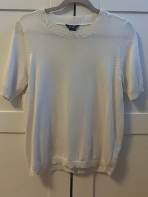 Vit stickad kortärmad tröja - En stilren vit stickad tröja med korta ärmar och rund halsringning. Tröjan har ribbade muddar vid ärmslut och nederkant, vilket ger en snygg och enkel look. Perfekt att matcha med jeans eller kjol för en snygg outfit. Pris kan diskuteras, kolla även om mina andra artiklar och skapa bundles!