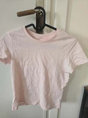 Ljusrosa t-shirt från Gina Tricot - En basic ljusrosa t-shirt från Gina Tricot i mjuk bomull. Klassisk rund halsringning och korta ärmar. Perfekt att matcha med jeans eller kjol för en enkel och clean look. Aldrig använd!