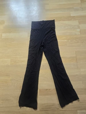 Svarta utsvängda leggings - Säljer ett par svarta yoga pants med nedvikbar midja och utsvängda ben. De är mjuka och stretchiga, perfekta för en avslappnad och trendig look. Materialet känns som bomull eller viskosblandning och de har en enkel, stilren design utan synliga detaljer. Storlekslappen bortklippt, men tror det är stl 146/152 