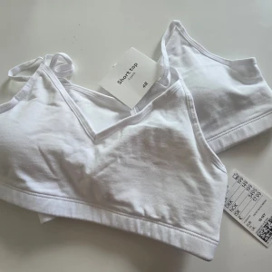 Vit mjuk bh med v-ringning från H&M - Stilren vit bh från H&M i mjuk bomull med smala axelband och v-ringad skärning. Enkel och bekväm design utan bygel, perfekt för en avslappnad look. Lappen sitter kvar.