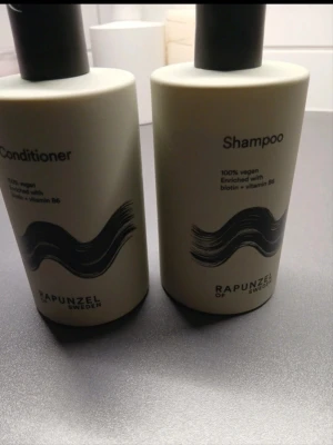 Shampoo och balsam Rapunzel of Sweden - Säljer ett set med shampoo och balsam från Rapunzel of Sweden. Båda är 100% veganska och berikade med biotin och vitamin B6. Flaskorna är vita med svart text och har en stilren design med vågigt mönster på framsidan.