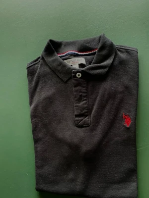 Svart pikétröja från US Polo Assn - Klassisk svart pikétröja från US Polo Assn tillverkad i bomull perfekt till sommaren. Aldrig använd 