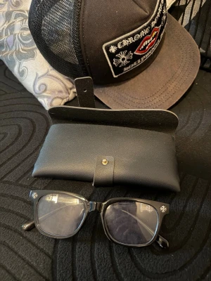 Svarta glasögon med silverdetaljer - Snygga svarta blå ljus glasögon från chrome hearts med fyrkantiga bågar och silverfärgade korsdetaljer på skalmarna. Kommer med ett svart fodral i läderimitation med knappstängning. Perfekt accessoar för en edgy och trendig look.