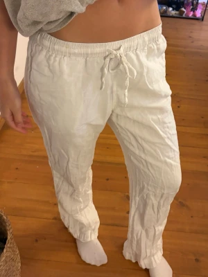 Vita linnebyxor med dragsko - Säljer ett par vita linnebyxor med avslappnad passform och elastisk midja med dragsko. Byxorna har raka ben och är tillverkade i ett lätt och luftigt linnetyg, perfekta för en chill och stilren look.