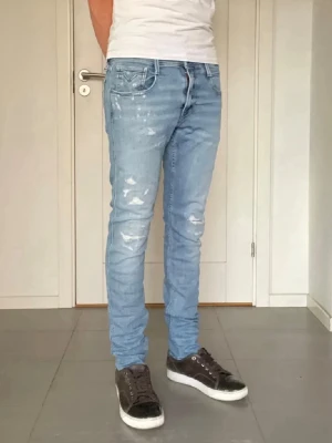 Replay Anbass jeans W32 L34 ljusblå slim fit - Replay Anbass jeans i W32/L34. Ljusblå tvätt med snygga slitningar/distressed detaljer och slim fit-passform. Jeansen är använda men i bra skick. Se bilder för skick och passform.  📏 W32 / L34 👖 Modell: Anbass 🎨 Ljusblå / washed ✨ Slim fit / distressed  Skicka gärna vid frågor eller om du vill ha fler mått/bilder.