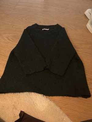 Mörgrön stickad tröja med trekvartsärm - Mysig mörkgrön stickad tröja med trekvartsärmar och rund hals. Tröjan har en rak passform och är tillverkad i ett mjukt, grovt stickat material som passar perfekt till kyligare dagar. 